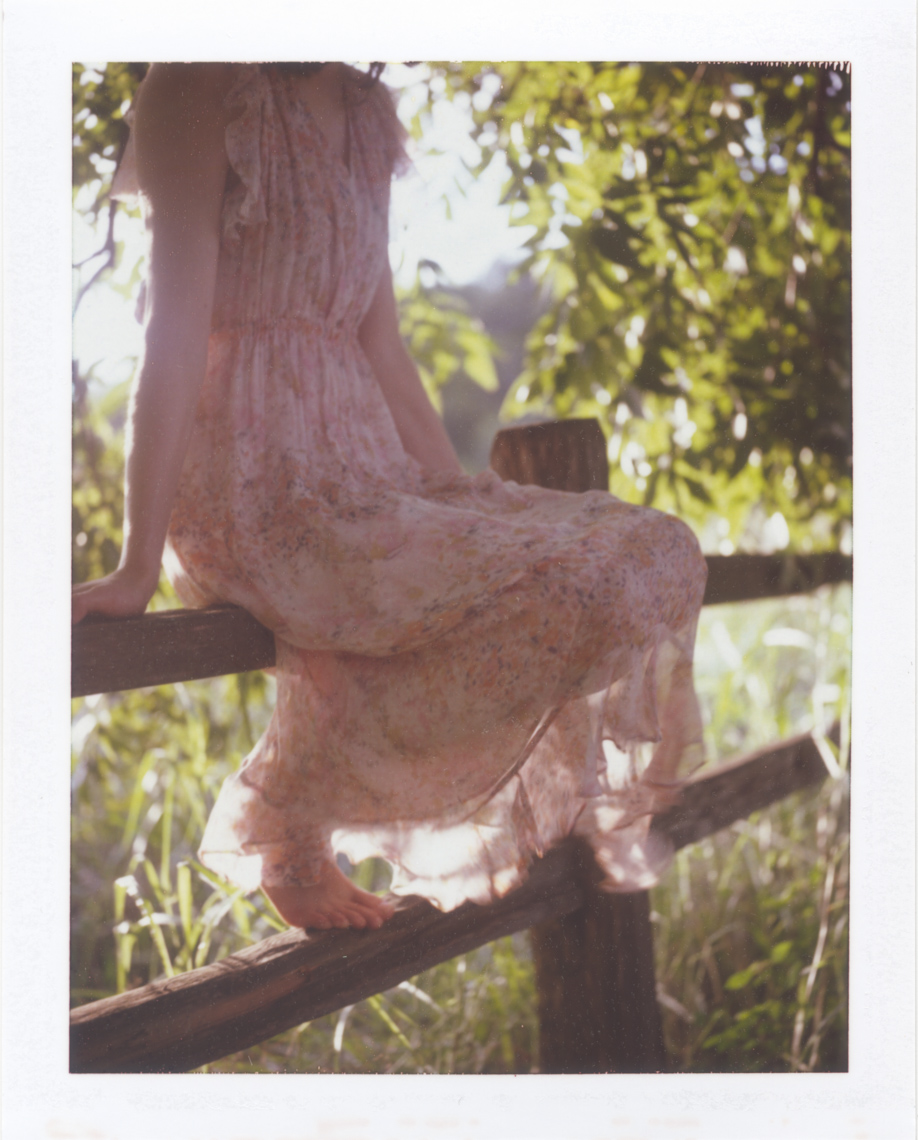 Pretty girl sitting on fence | Photographer using Polaroid
